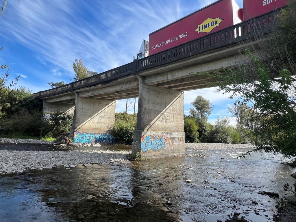 A truck drives over the Ohau River bridge, showing graffiti underneath