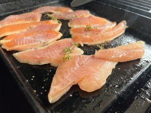 Trout fillets cooking on a BBQ hotplate, with a sprinkle of fresh thyme