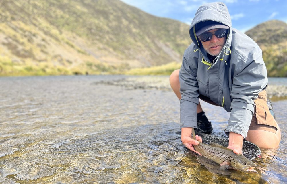 Teo releasing a nice Wainuiomata River brown trout, hood up against the wind.